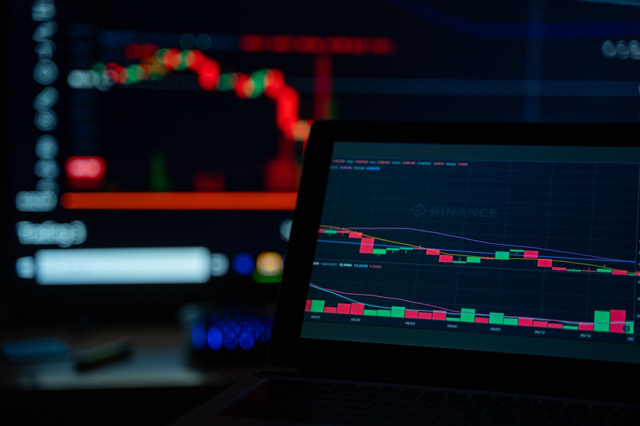 Un escritorio con iluminación tenue que muestra gráficos de operaciones con criptomonedas en varias pantallas.